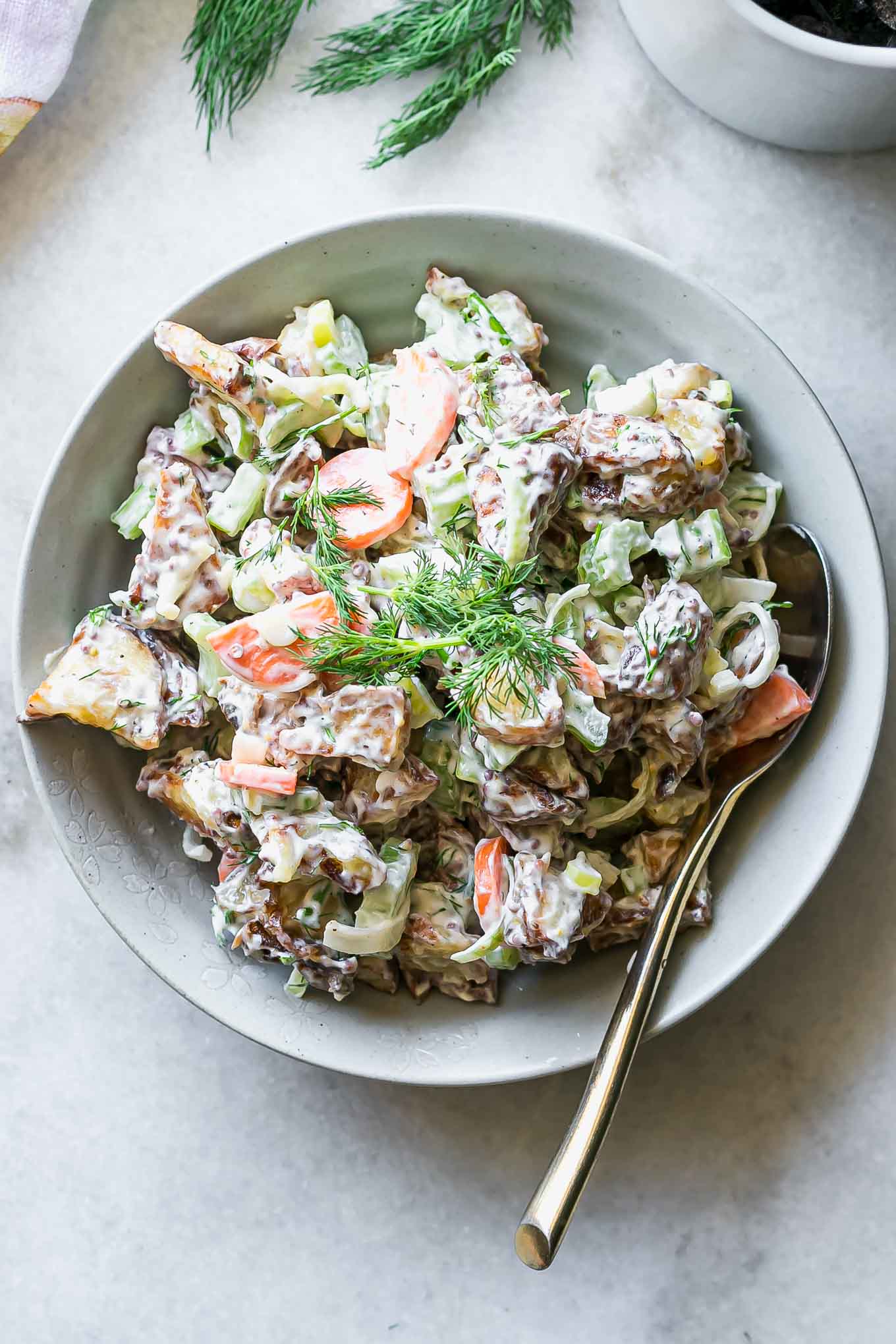 a bowl of potato salad with roasted potatoes on a white table