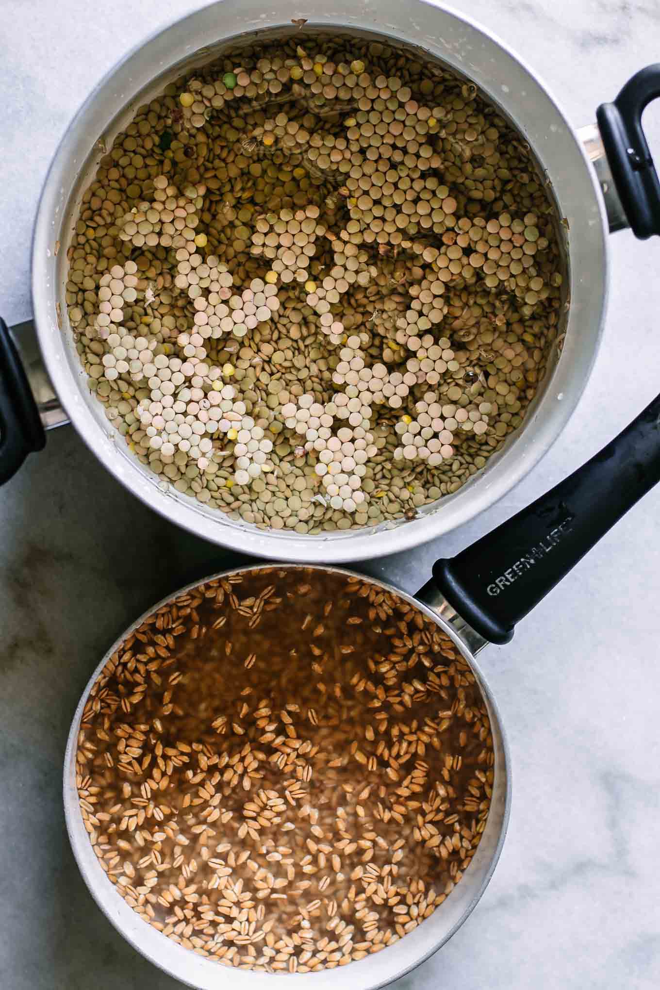 two pots with cooked lentils and cooked farro on a white table