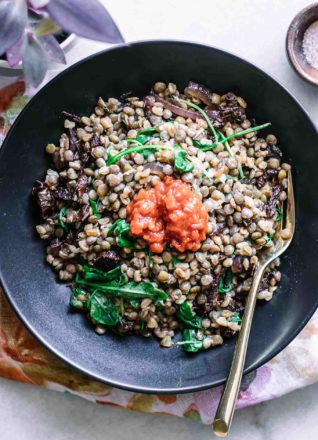 a black bowl with lentils, farro, and red harissa on a white table