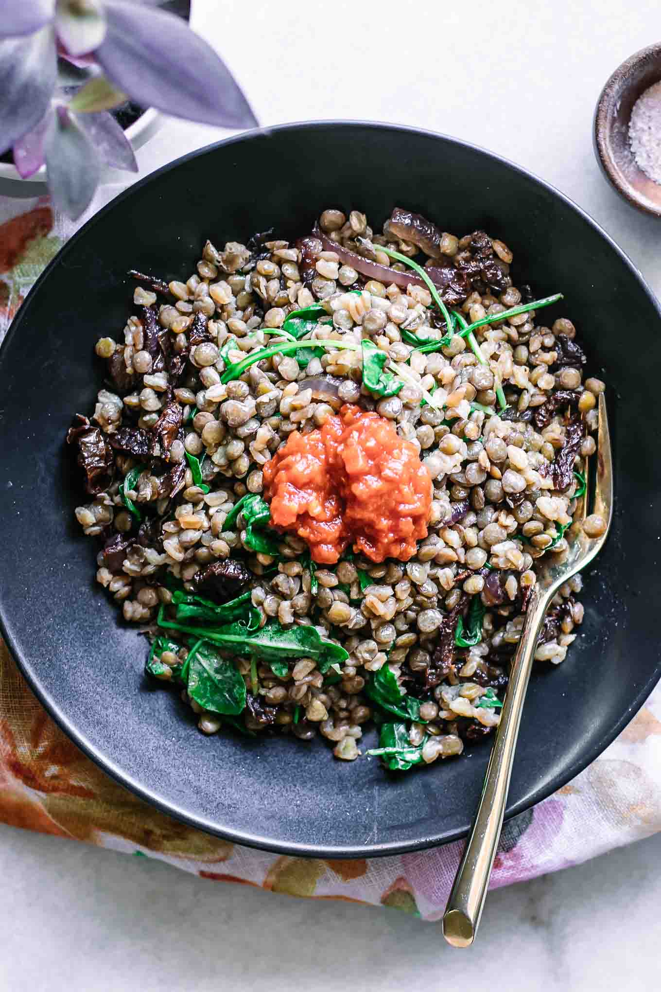 a black bowl with lentils, farro, and red harissa on a white table