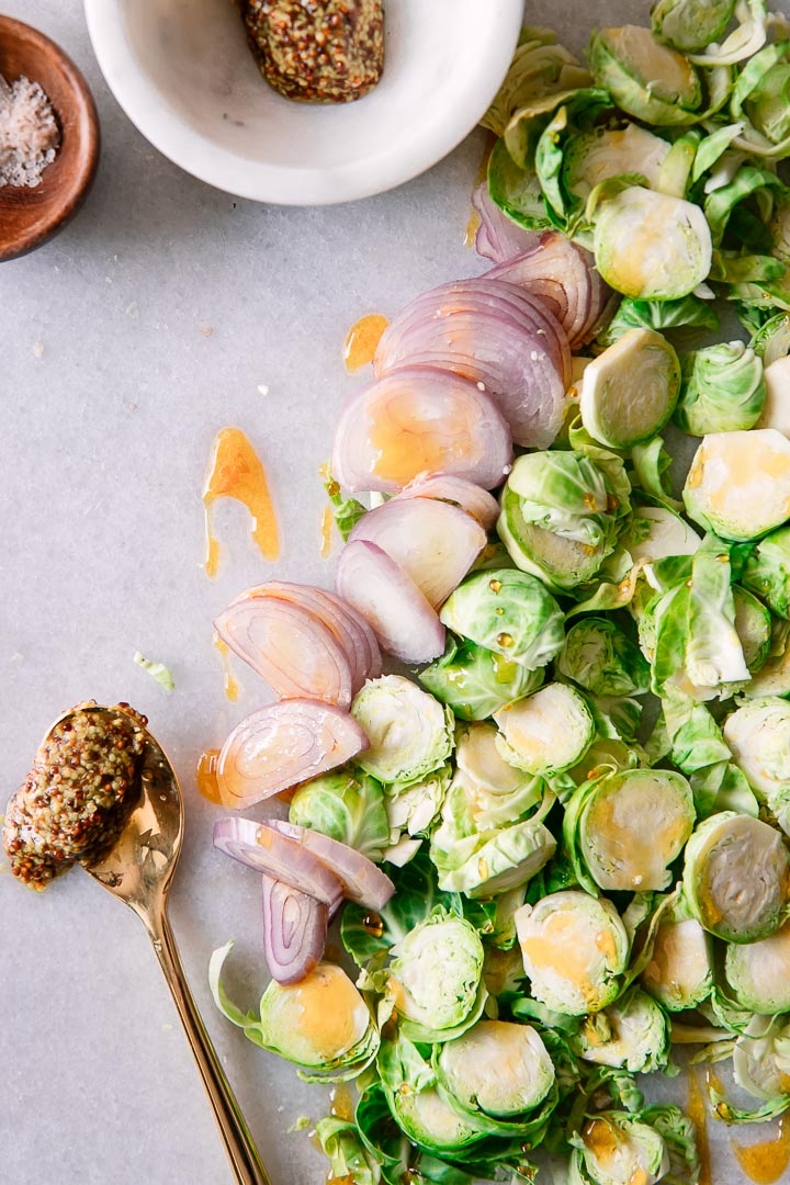 shredded brussels sprouts, sliced shallots, and mustard on a white cutting board