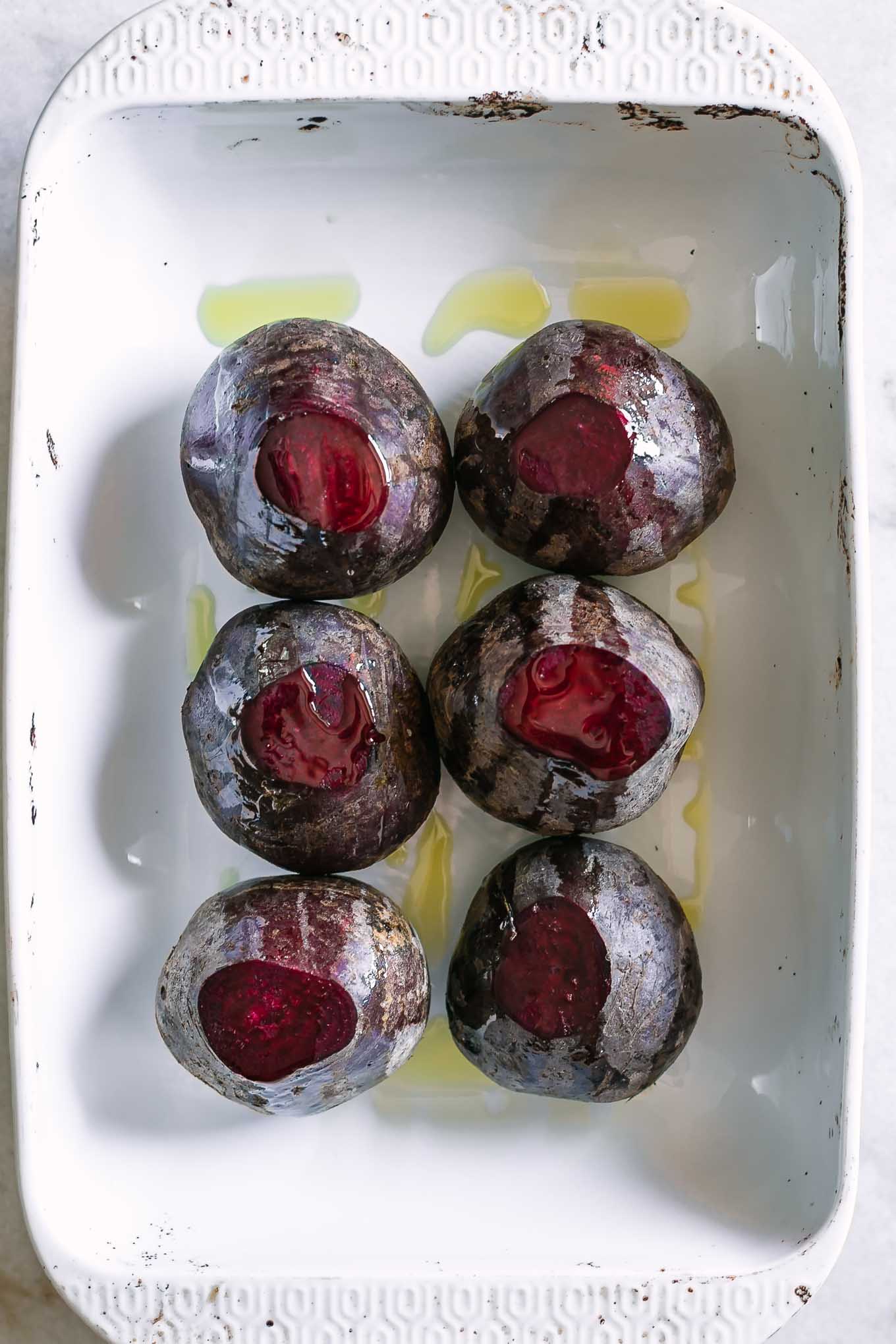 red beets and olive oil in a white roasting pan before baking