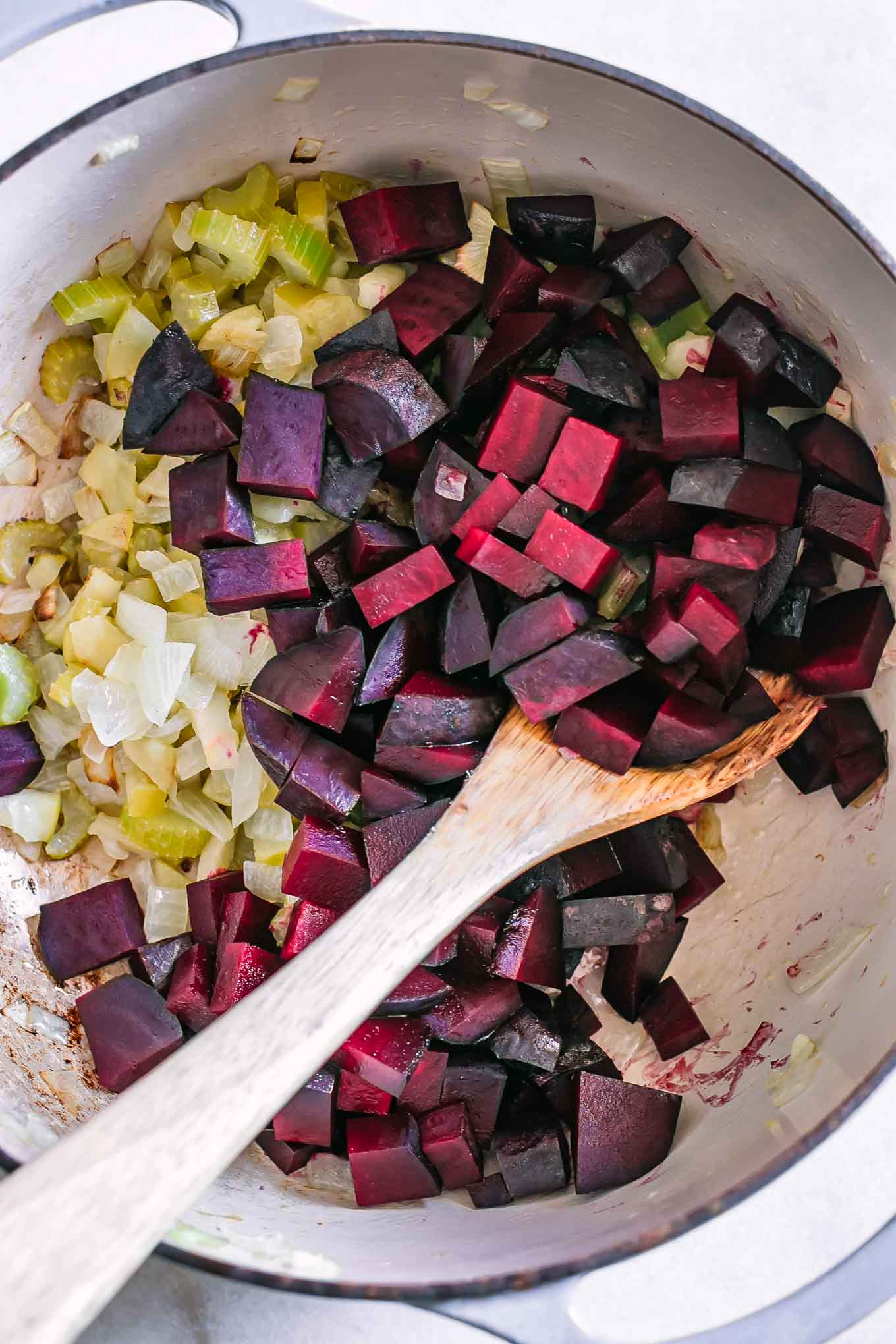 a soup pot with roasted beets, celery, onions, and apples with a wooden spoon