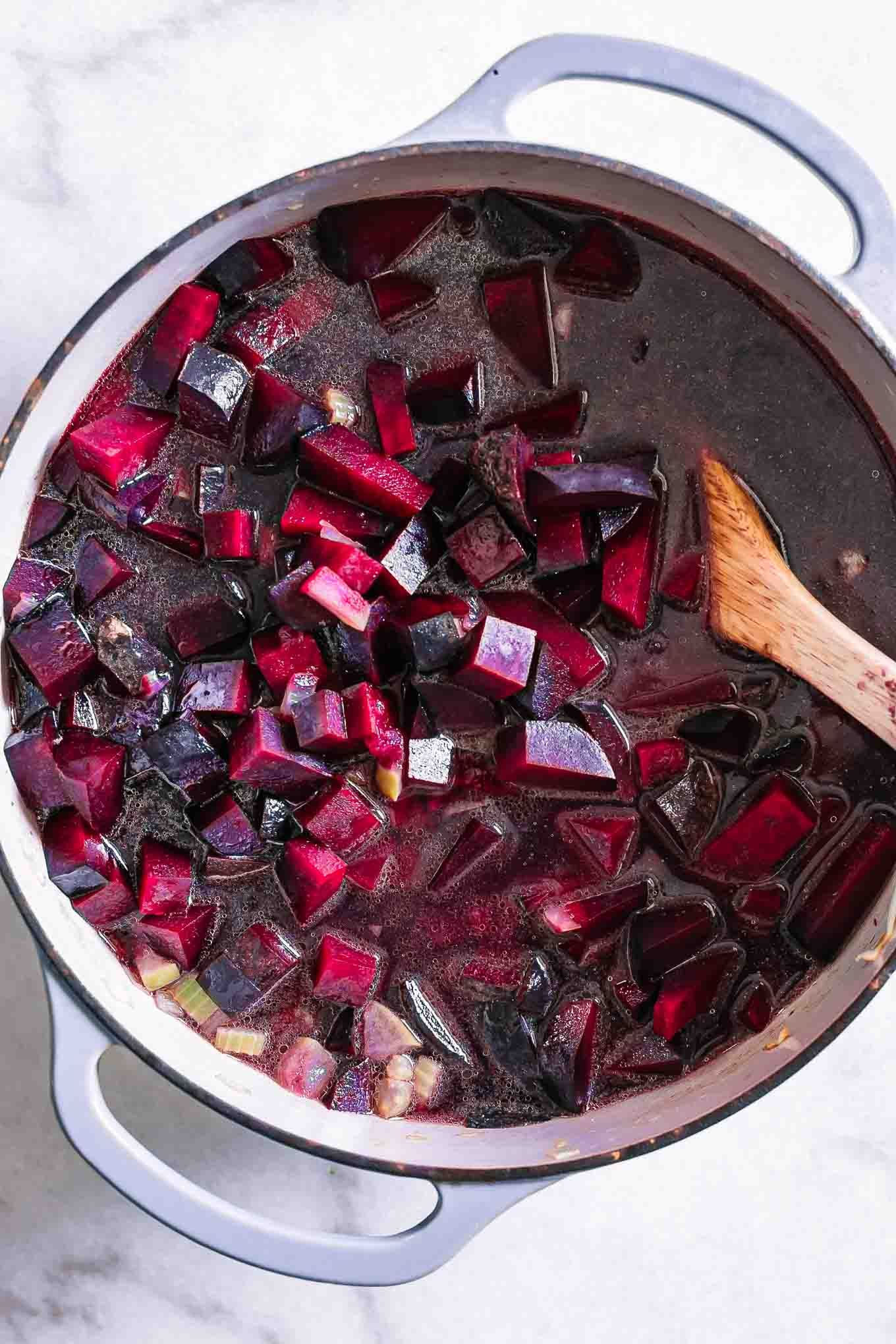 a pot of soup with broth and red beets and a wooden spoon