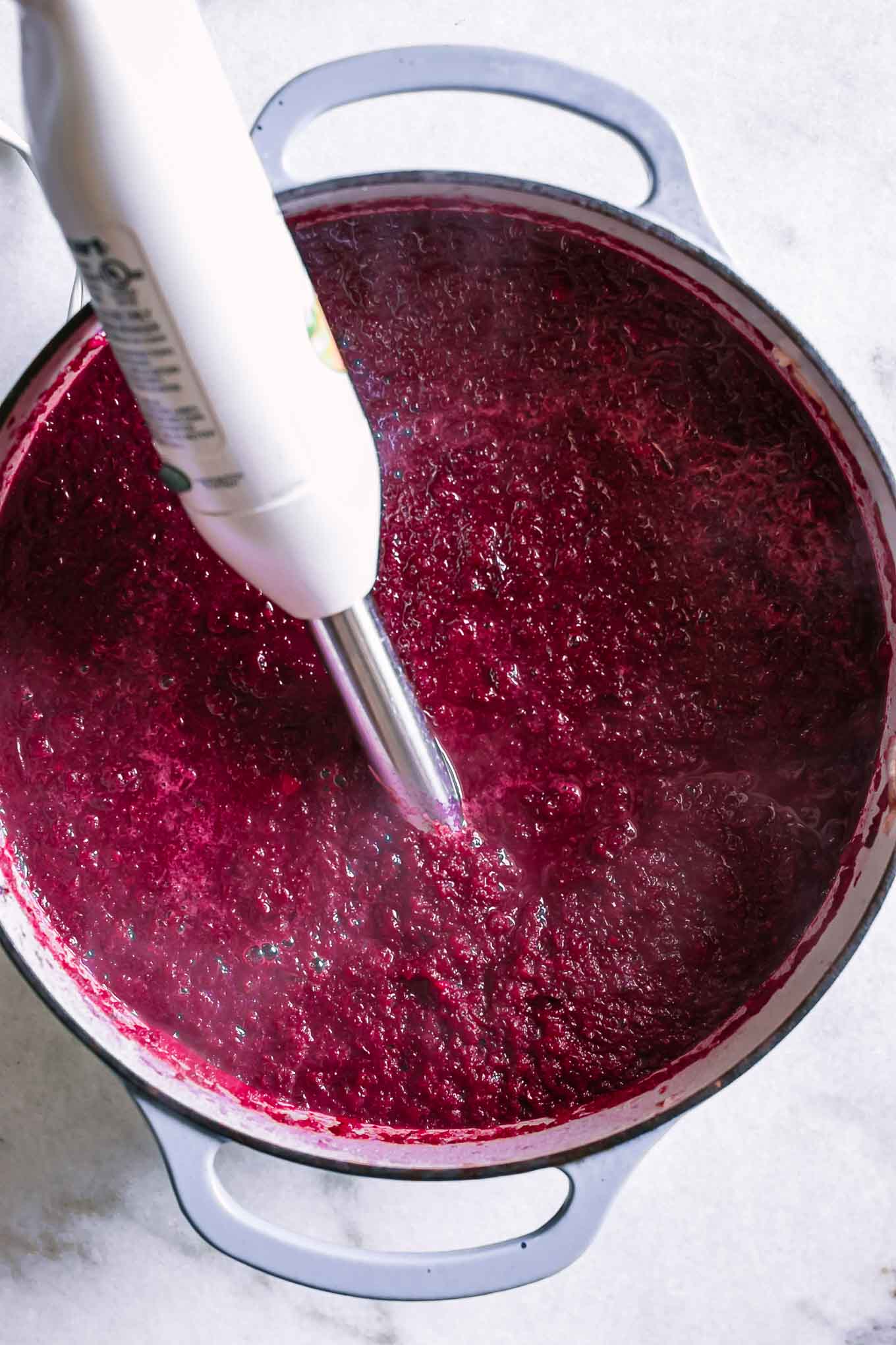 an immersion blender inside red beet soup in a large soup pot