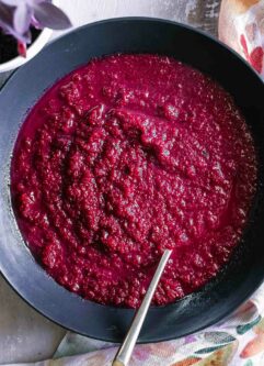 a roasted red beet and apple soup in a black bowl with a gold fork