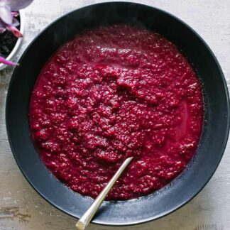 a bowl of red beet apple soup on a wood table with a gold fork