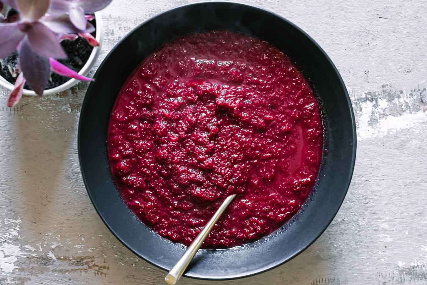 a bowl of red beet apple soup on a wood table with a gold fork