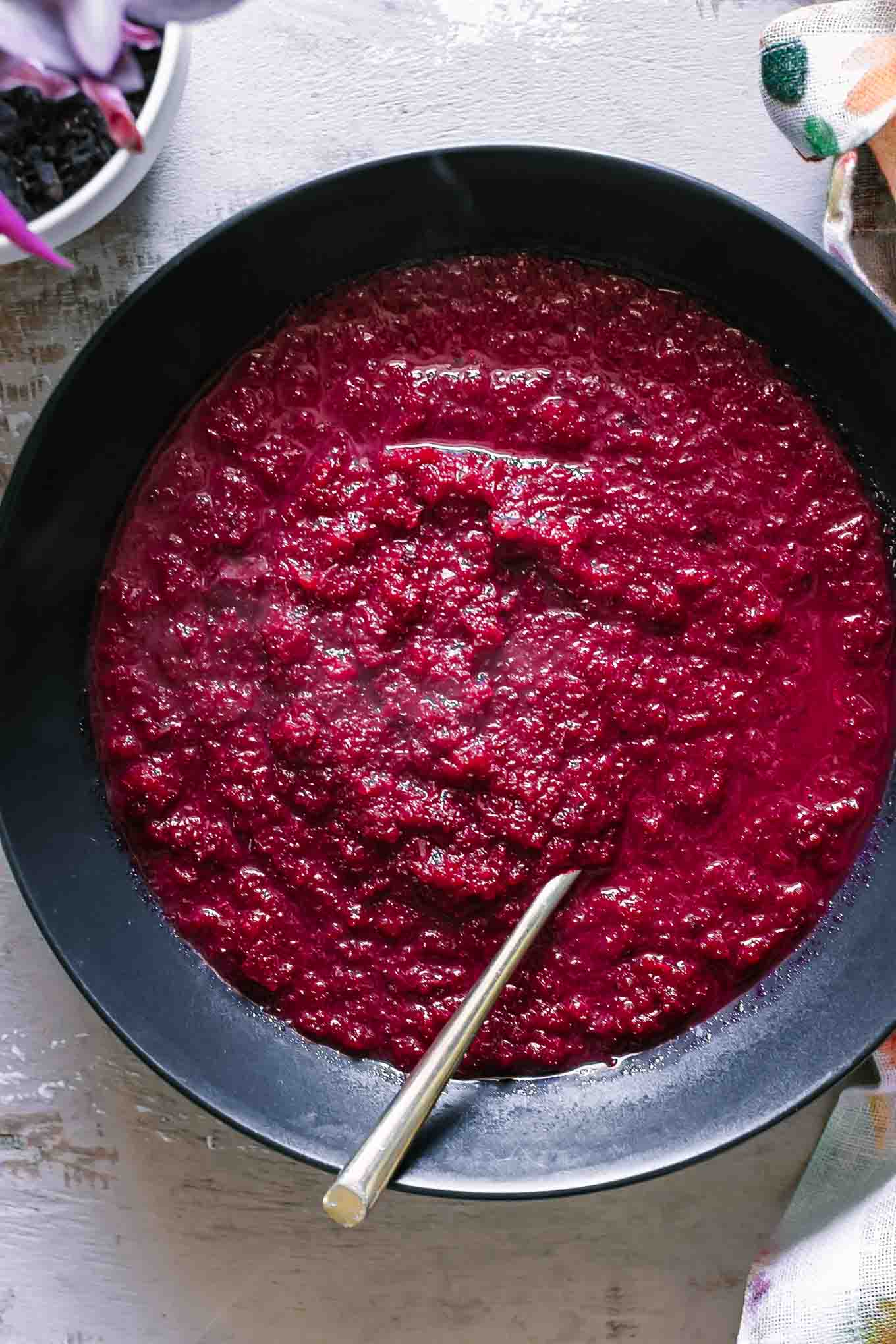 a black bowl with beet and apple soup with a gold fork