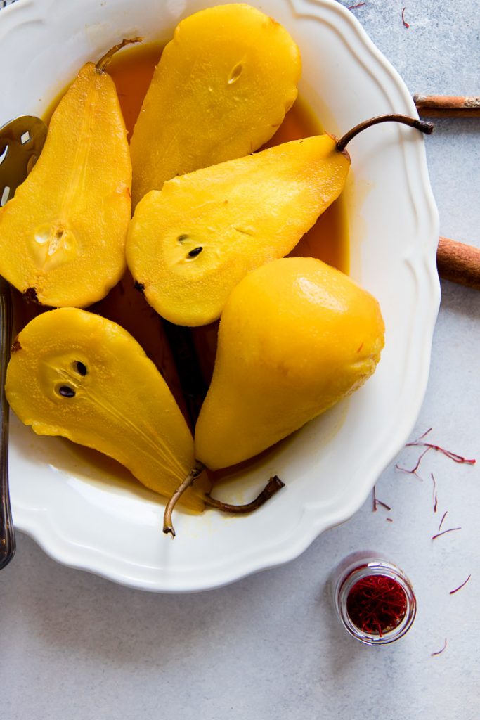 a plate of sliced poached pears with saffron sauce on a table with cinnamon sticks and red saffron threads