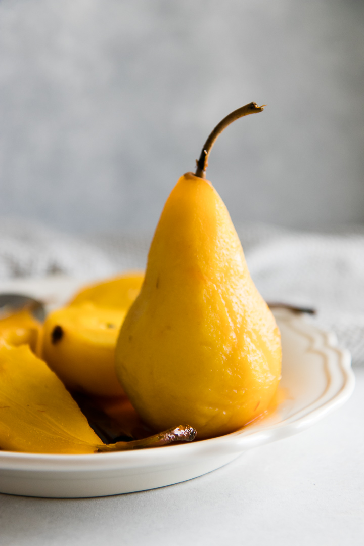 A yellow poached pear on a white plate on a white table