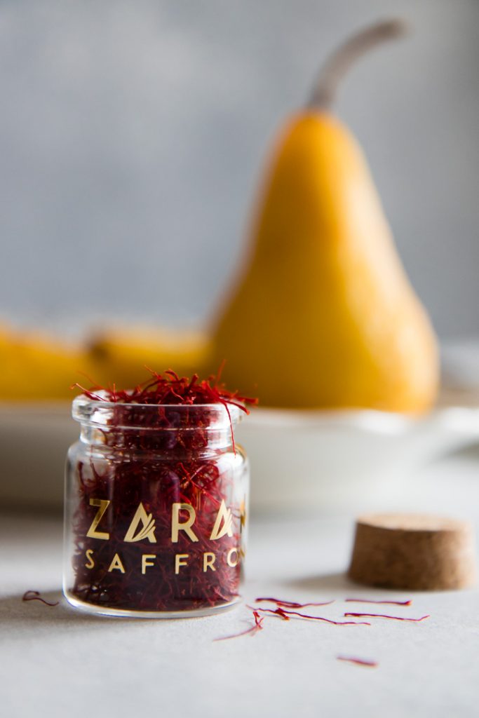 red saffron threads in a small glass jar on a blue table with pears in the background