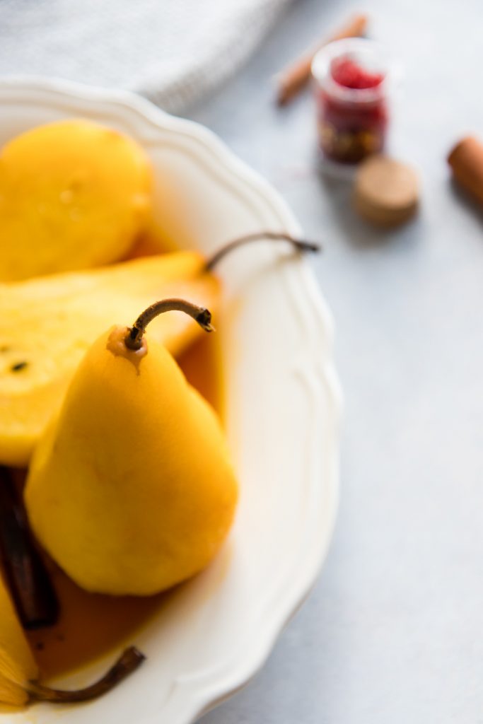 a poached pear on a white plate with a bowl of red saffron in the background