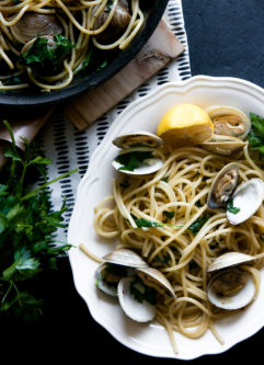 Pasta with clams on a white plate on a black table.
