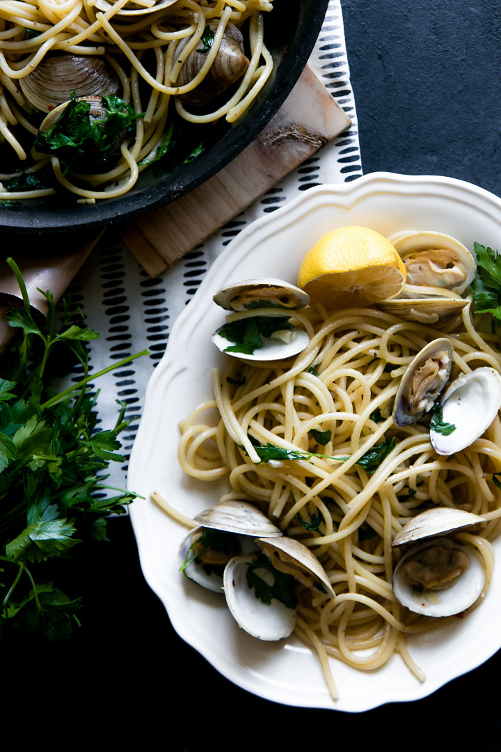 Pasta with clams on a white plate on a black table.