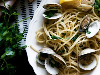 a plate of bucatini pasta with clams, lemons, and parsley on a white plate