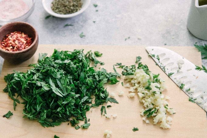 chopped carrot leaves, garlic, and red pepper on a cutting board with a knife