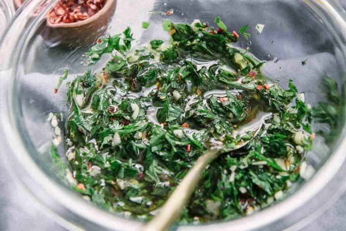 chimichurri sauce in a glass bowl with an gold spoon