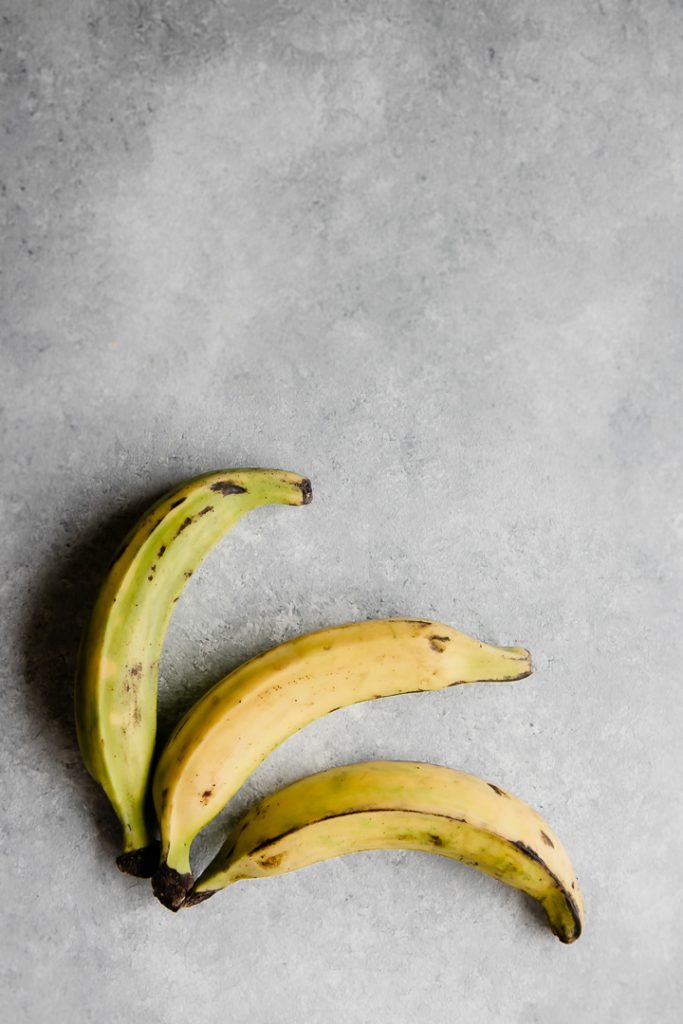 three plantains on a grey blue table for healthy baked patacones