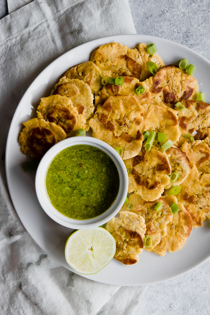 patacones healthy baked smashed plantains on a white plate with green mojo sauce