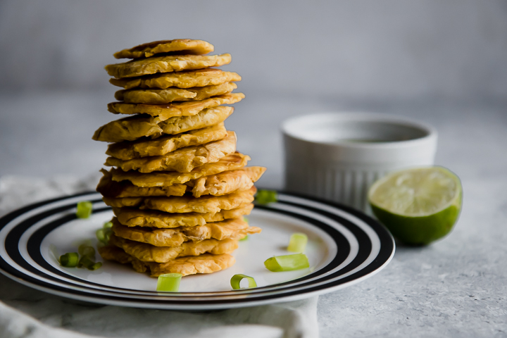 stacked patacones smashed plantains on a white plate with green mojo sauce