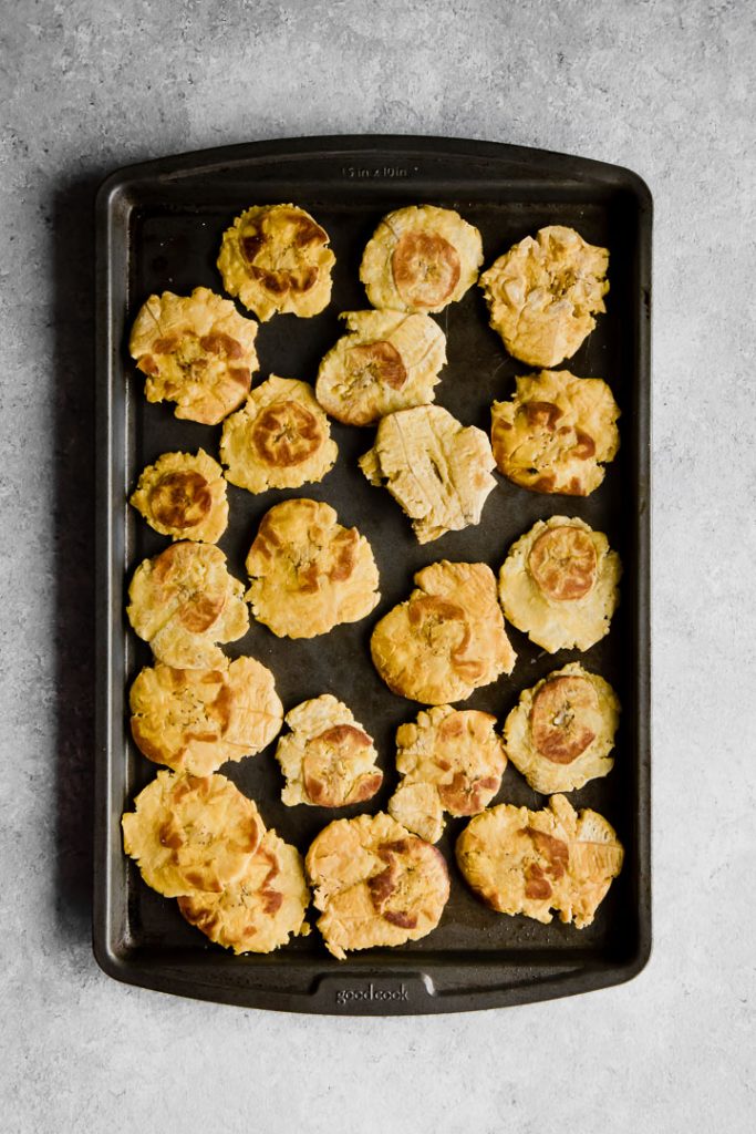 healthy baked patacones, or smashed plantains, on a black cookie sheet