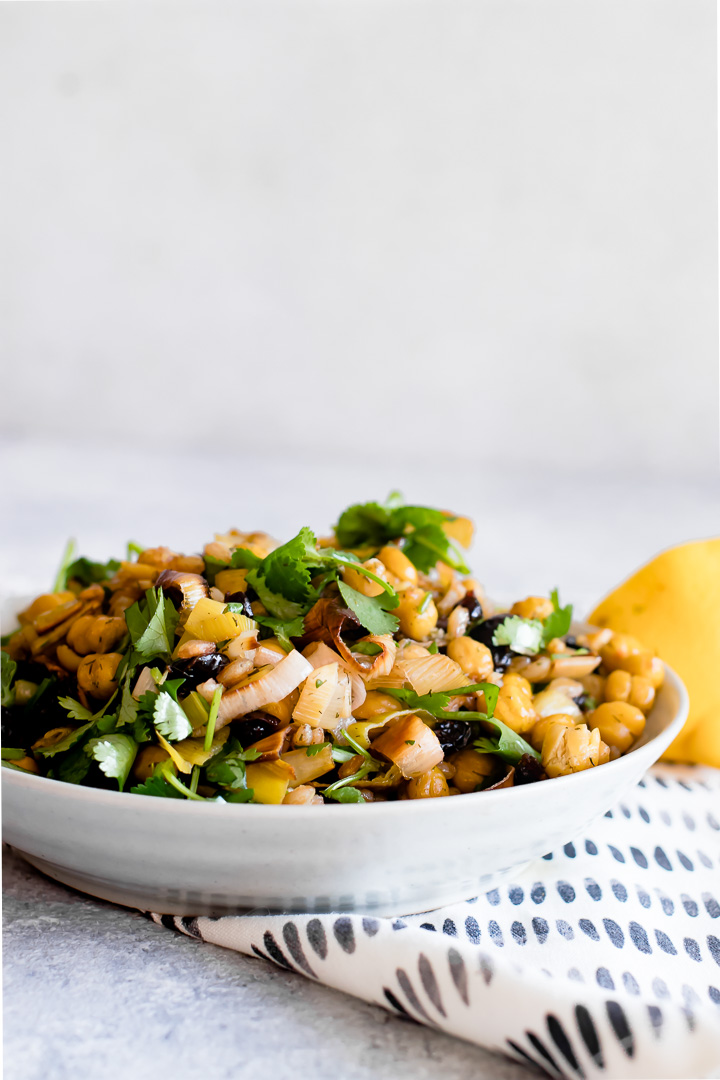 za'atar crispy chickpea and leek salad in a white bowl on a blue table with a white napkin and a side of lemon