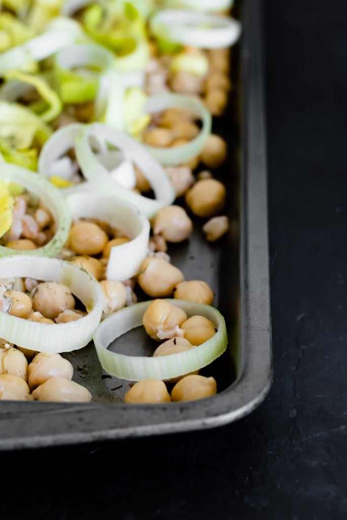 a sheet pan with chickpeas and sliced leeks on a black table