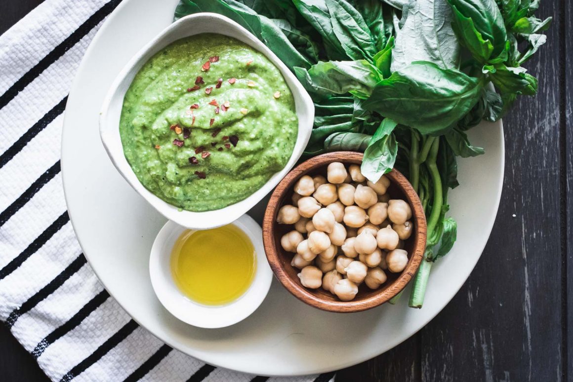 Nut-free chickpea basil pesto on a white plate on a wooden table with a napkin.