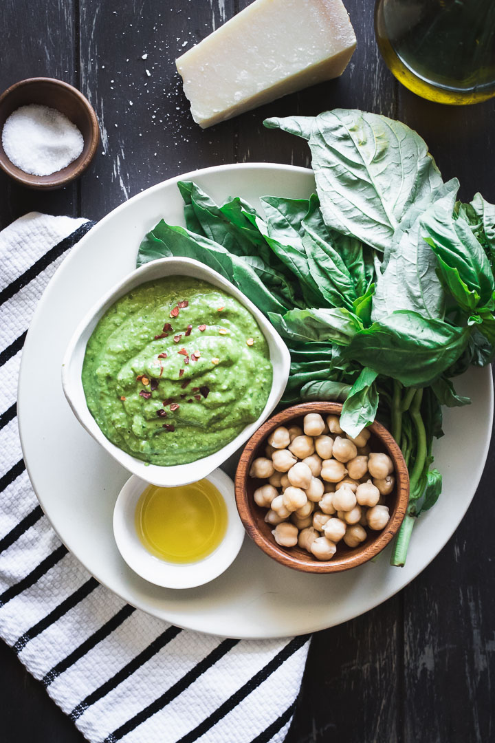 Nut-free chickpea basil pesto on a white plate on a wooden table with a napkin.