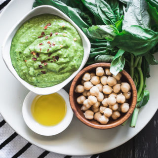 Nut-free chickpea basil pesto on a white plate on a wooden table with a napkin.