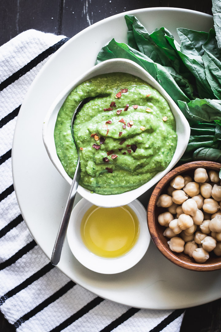 chickpea pesto in a white ramekin on a white plate with a silver spoon