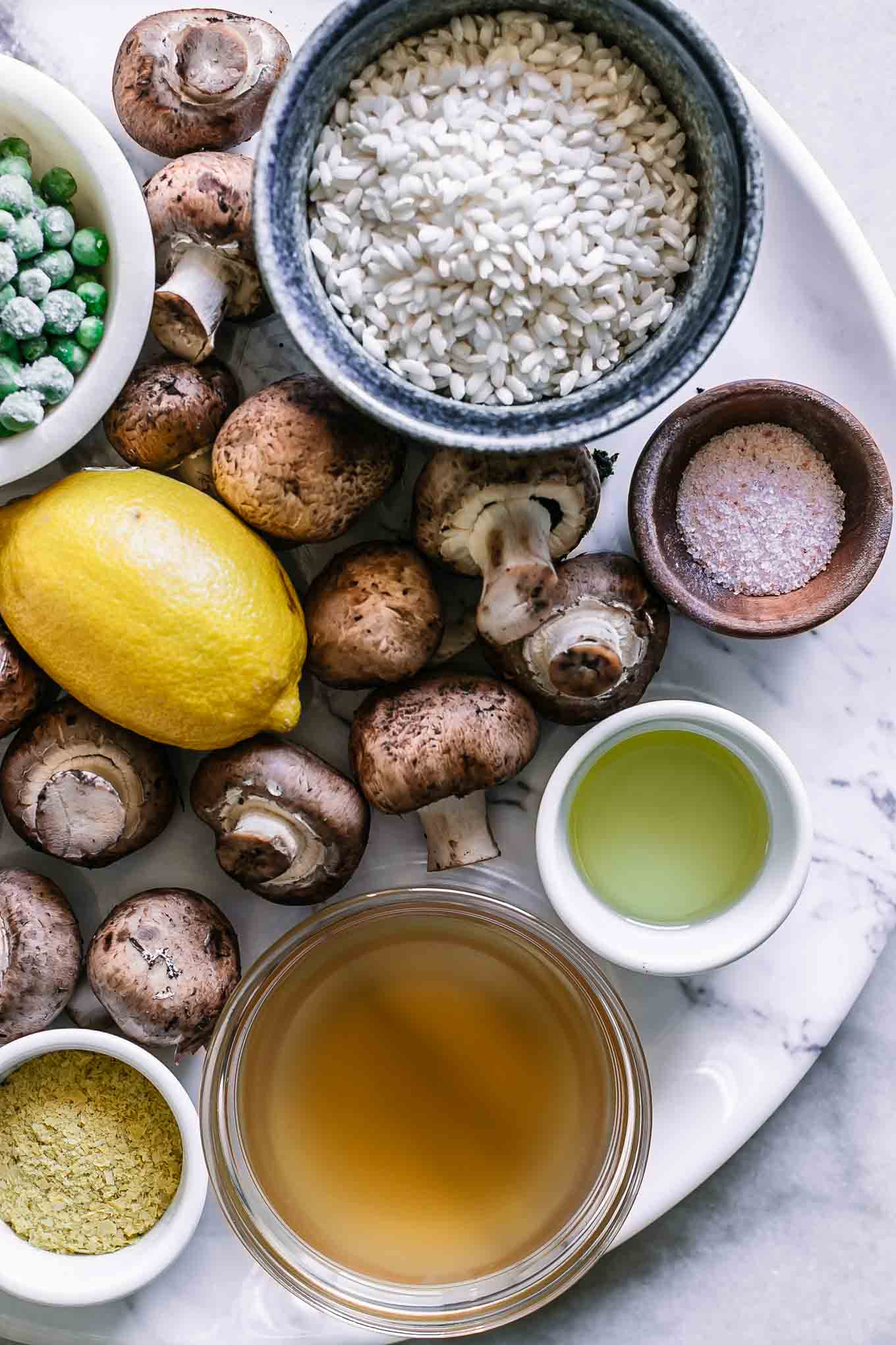 mushrooms, truffles, lemon, pea, arborio rice, broth, and oil on a white table for risotto