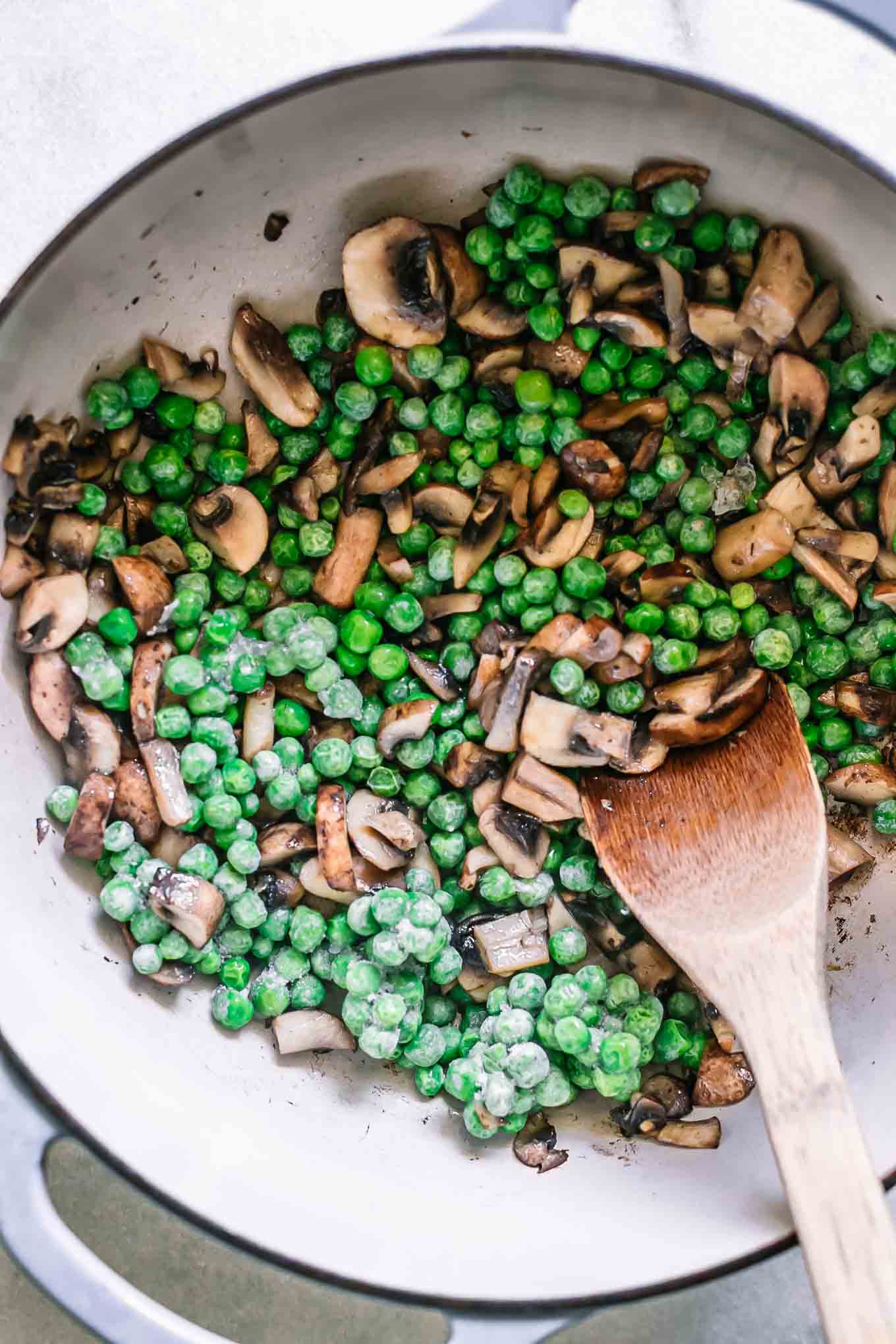 cooked mushrooms and peas in a pot with a wooden spoon