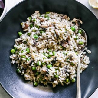 risotto with mushrooms, peas, and truffle oil in a black bowl with a gold fork
