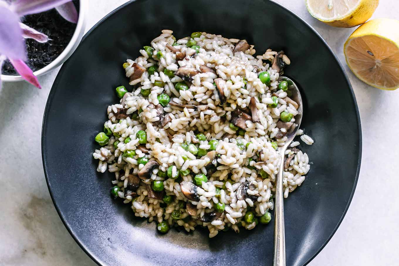 risotto with mushrooms, peas, and truffle oil in a black bowl with a gold fork