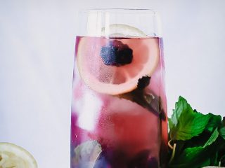 A glass of boozy blackberry lemonade on a cutting board with fresh fruit.