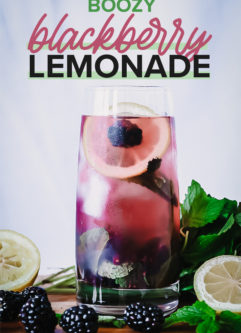 a glass of lemonade with blackberries and lemons inside on a wooden table with a blue background and the words "boozy blackberry lemonade" in purple and black writing