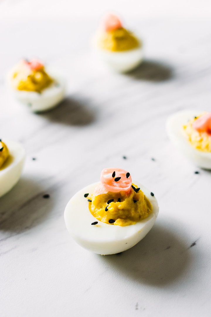 A wasabi ginger deviled eggs with pickled ginger on top on a slab of marble garnished with black sesame seeds.