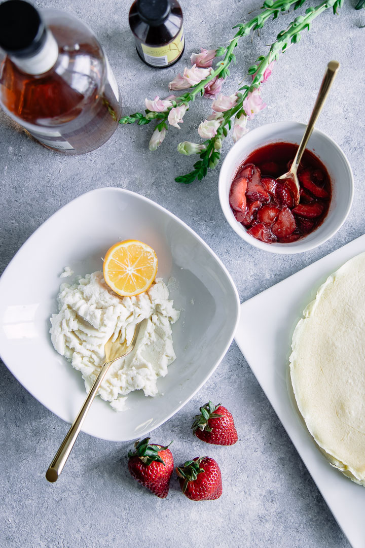 A crepe with ricotta and vanilla bourbon strawberries on a white plate on a blue table with flowers.