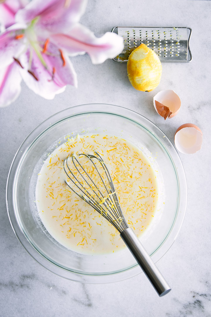 Dutch baby pancake batter on a table with a Meyer lemon and pink flowers.