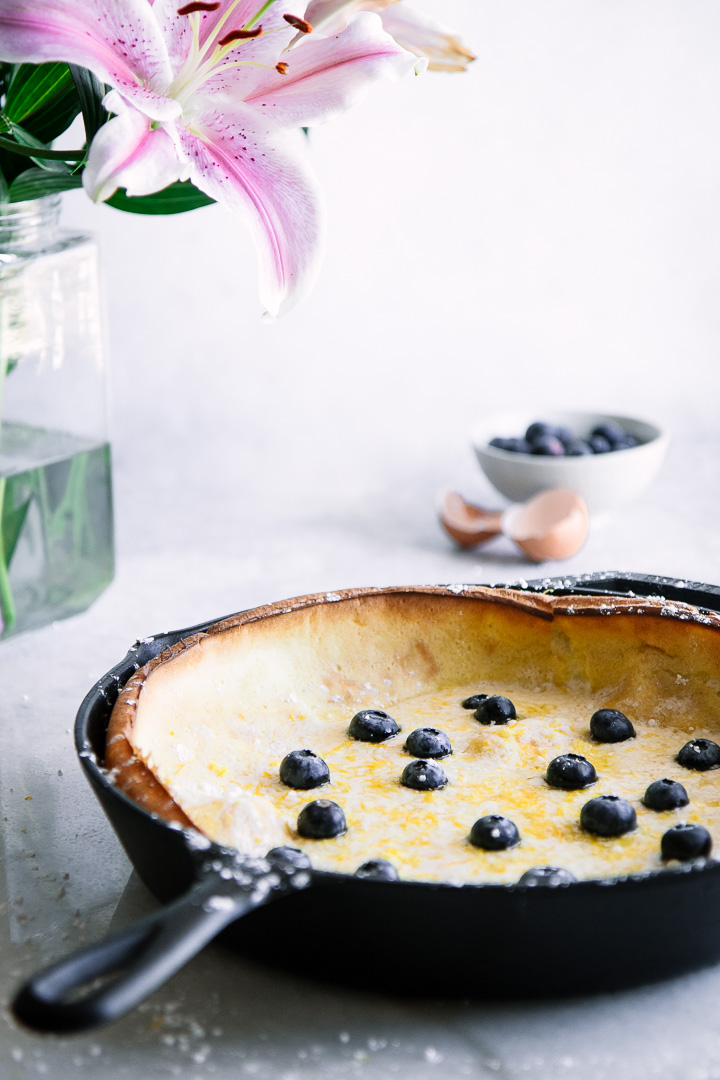 Dutch baby pancake with blueberries in a cast iron skillet on a blue table with pink flowers.