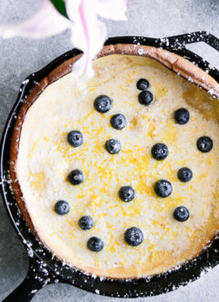 Dutch baby pancake with blueberries in a cast iron skillet on a blue table with pink flowers.