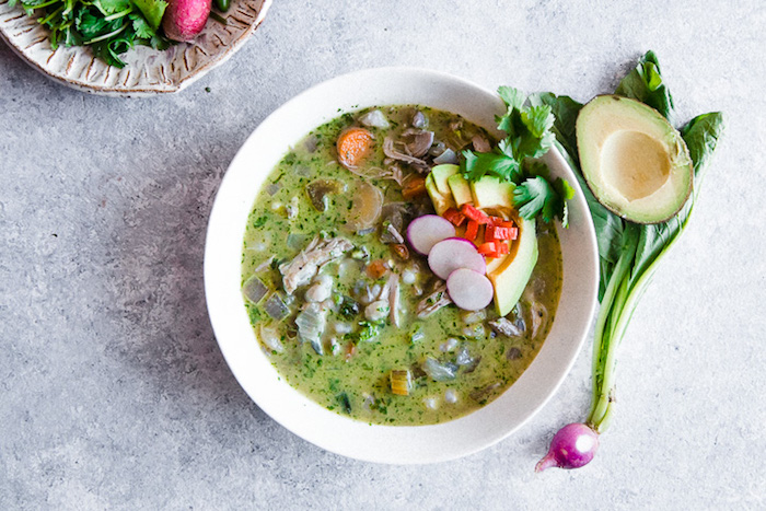 A white bowl of pozole verde soup on a blue table.