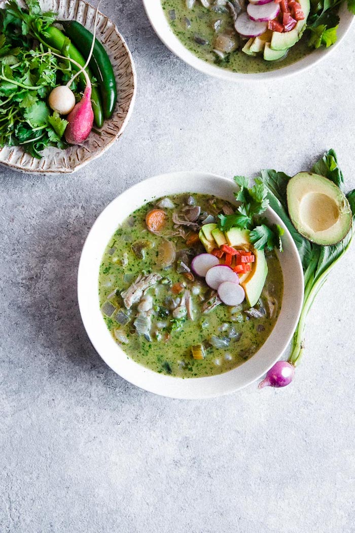 A white bowl of pozole verde soup on a blue table.