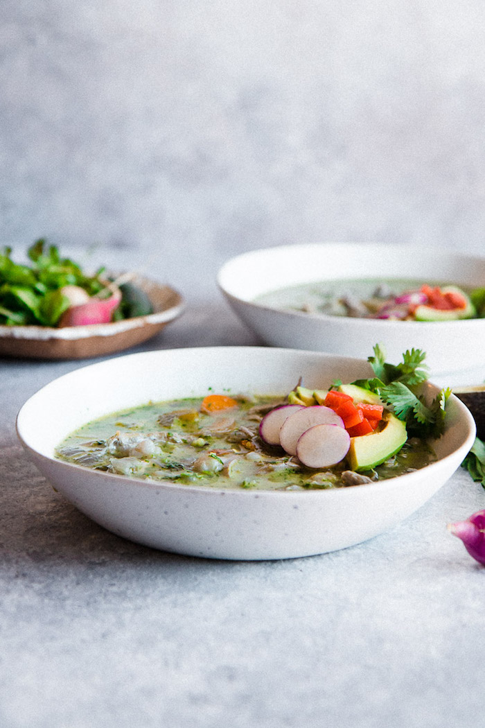 Three bowls of pozole verde soup on a blue table.