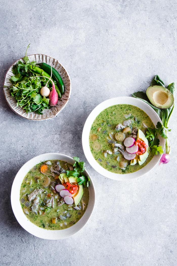 Three bowls of pozole verde soup on a blue table.