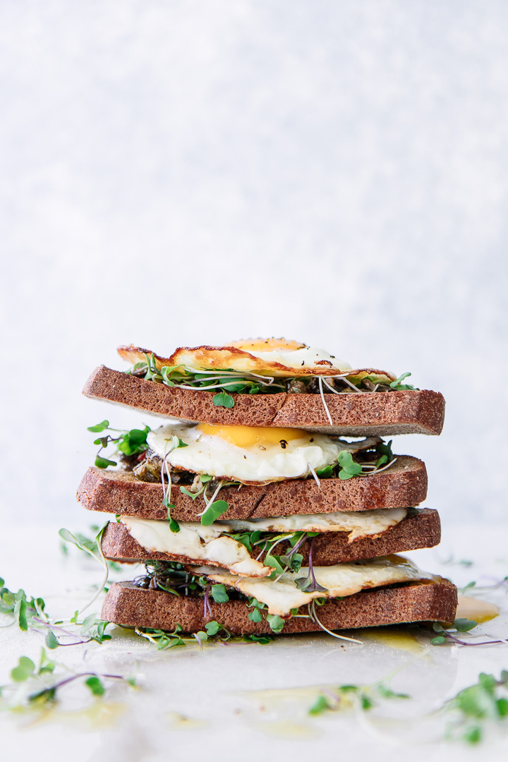 Stacked pieces of bread with olive tapenade, olive oil, microgreens, and sunny eggs on a piece of marble.
