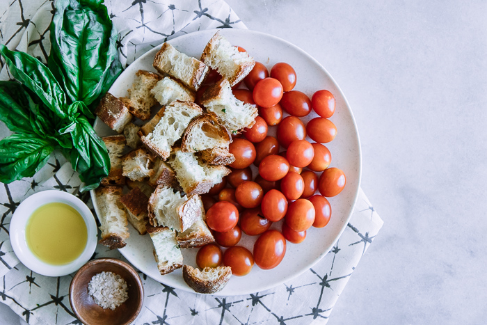 Tomatoes, ciabatta bread, and fresh basil on a white plate on a white table.