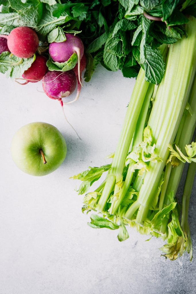 Celery, an apple, and radishes on a white table.